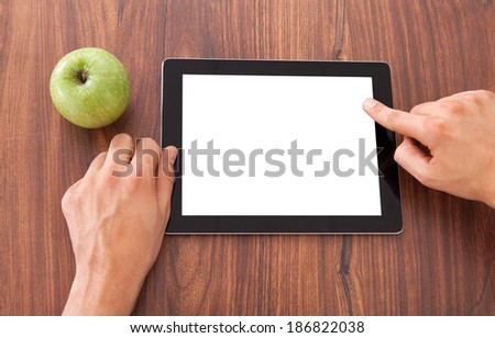 Cropped image of male college student using blank digital tablet by green apple on table