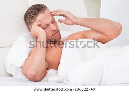 Man waking up with a nasty headache from overindulgence or illness wincing in pain and raising his hands to his head