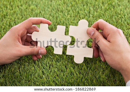Cropped image of hands connecting two puzzle pieces on grass