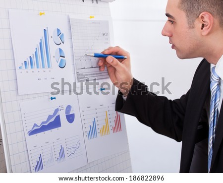 Side view of young businessman analyzing graph with pen in office