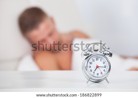 Alarm clock about to ring in the morning showing a quarter past seven with a man sleeping in bed in the background  focus to the clock