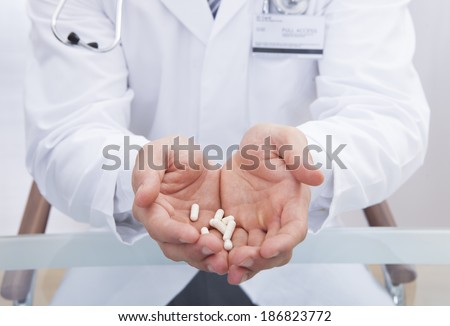 Doctor or male nurse in a white lab coat holding tablets in his cupped hands offering them to the viewer  close up view of his hands