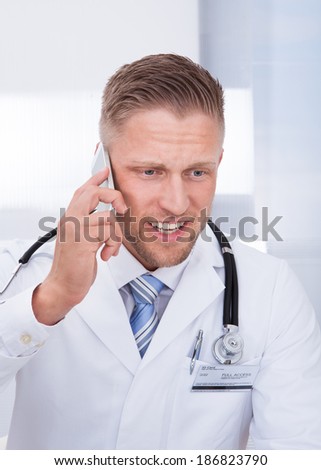 Friendly doctor chatting on his mobile phone smiling as he listens to the conversation  close up of his face
