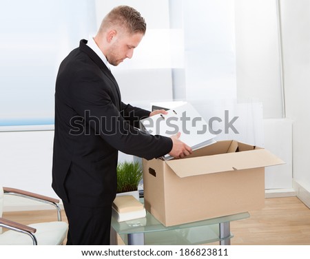 Businessman moving offices packing up all his personal belongings and files into a brown cardboard box