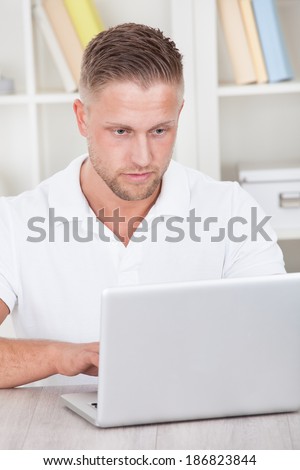 Young man in a short sleeved shirt sitting working at home on a laptop in a home office