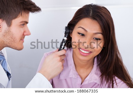Side view of male doctor examining patient\'s ear with otoscope in clinic