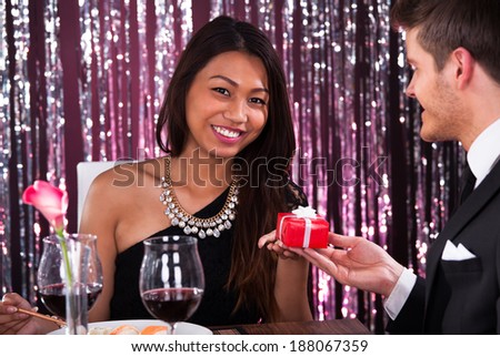Portrait of happy young woman receiving gift from man in restaurant