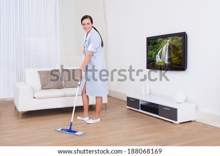 Full length portrait of young maid cleaning floor with mop at home
