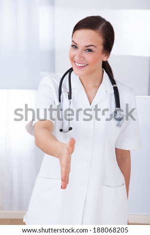 Portrait of happy young female doctor offering handshake in hospital