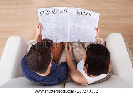 High angle view of young couple reading newspaper together on sofa at home