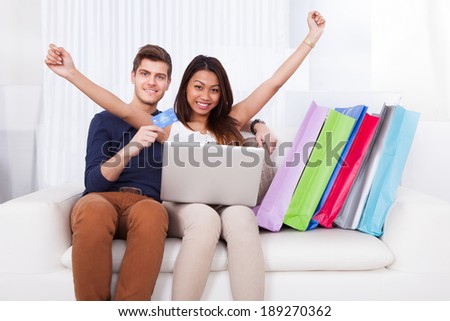 Portrait of happy young couple shopping online with bags on sofa at home