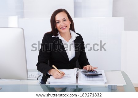 Portrait of happy businesswoman calculating tax at desk in office