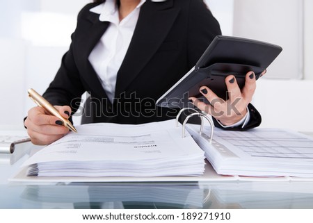 Midsection of female accountant calculating tax at desk in office