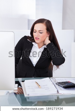 Young female tax consultant suffering from neck pain sitting at desk in office