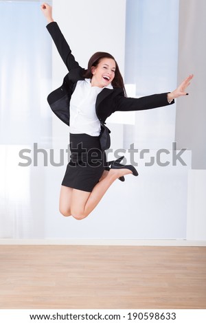 Full length of excited young businesswoman jumping in office