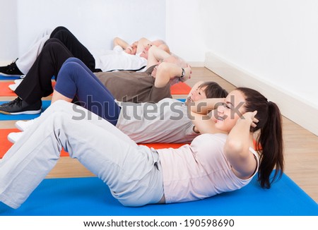 Female trainer and senior customers doing sit ups on exercise mats at gym