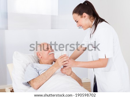 Happy female doctor giving glass of water to senior man in hospital