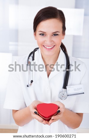 Portrait of happy young female doctor holding heart in hospital