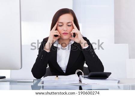 Tensed young businesswoman calculating tax at desk in office