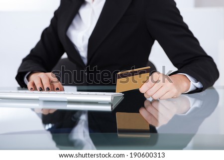 Midsection of businesswoman holding credit card at desk in office