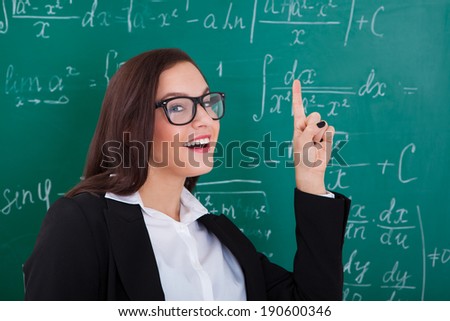 Portrait of happy young teacher pointing at chalkboard in math class