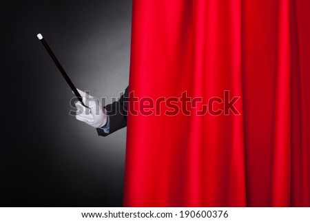 Cropped image of magician holding wand behind stage curtain