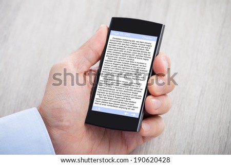 Closeup of businessman\'s hand displaying eBook on smartphone at desk