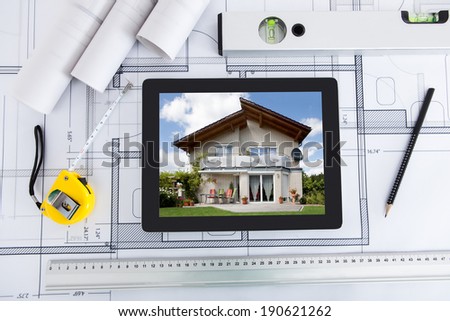 House displayed on digital tablet screen with architect\'s tools over blueprint