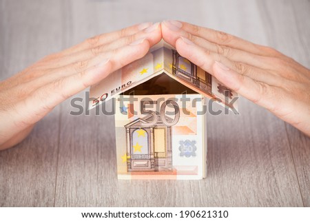 Closeup of businessman\'s hands protecting euro house on table