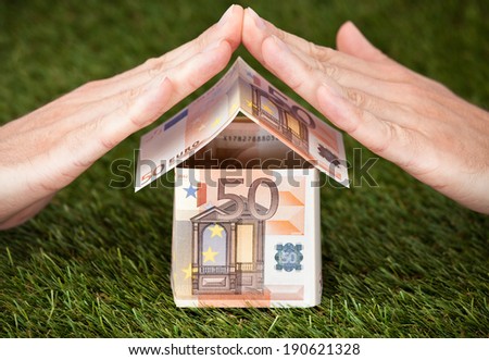 Businessman\'s hands protecting house made of euro notes on grassy land