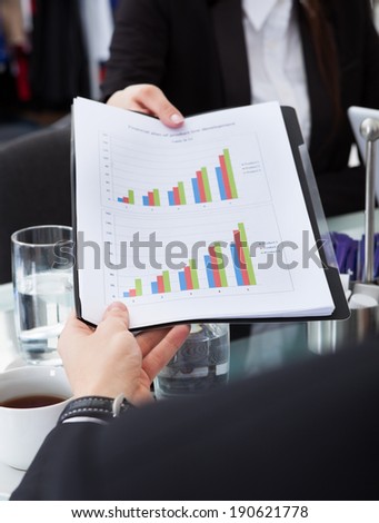 Cropped image of businesswoman giving progress chart to colleague at desk in office