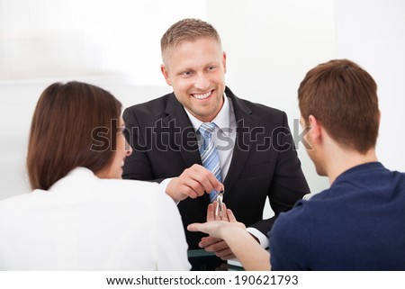 Happy estate agent giving house keys to young couple in office