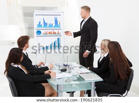 Businessman writing on flipchart while giving presentation to colleagues in office