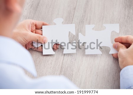 Cropped image of businessman joining jigsaw pieces at desk