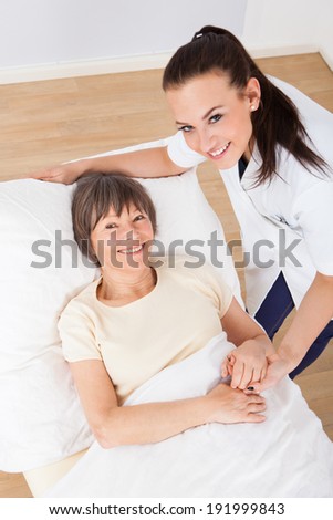 Portrait of happy female doctor consoling senior woman lying in bed at clinic