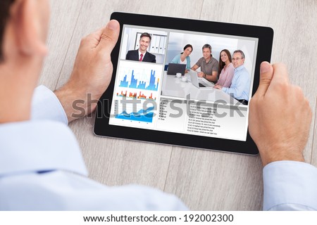 Cropped image of businessman video conferencing with team on digital tablet at desk in office