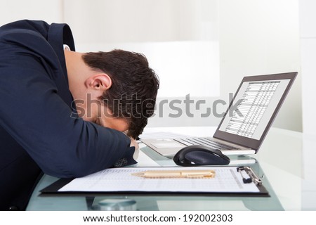 Side view of tired businessman sleeping while calculating expenses at desk in office
