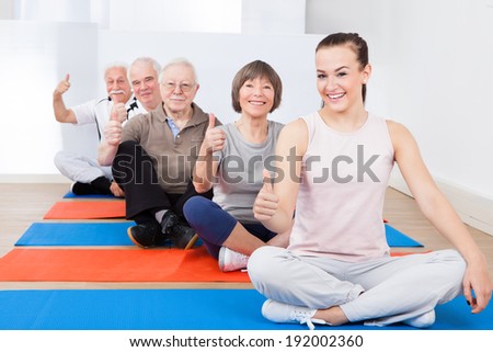 Portrait of confident trainer with senior customers sitting on exercise mat at gym