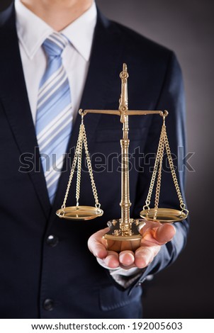 Midsection of businessman holding justice scale against black background