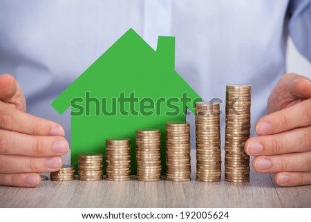 Midsection of businessman\'s hands protecting stacked euro coins and house model in office
