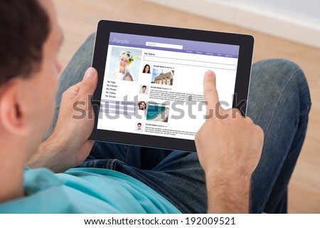 Mid adult man surfing on social site using digital tablet at home