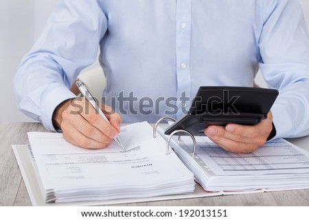 Midsection of businessman calculating financial expenses at desk