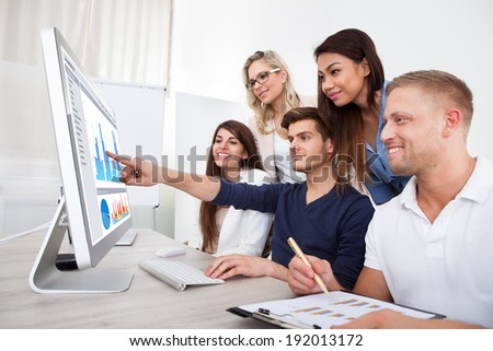 Group of smiling businesspeople using desktop PC together in office