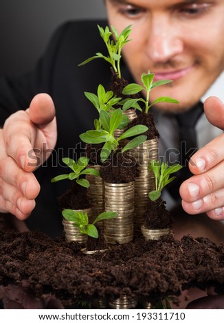 Young businessman protecting coins in saplings representing responsible business against black background