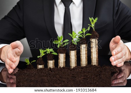 Midsection of businessman\'s hands protecting coins in saplings representing responsible business