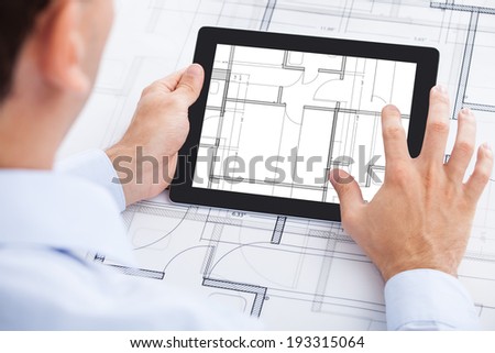 Cropped image of architect analyzing blueprint on digital tablet in office