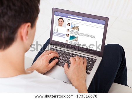 Midsection of man using social networking site on laptop at home
