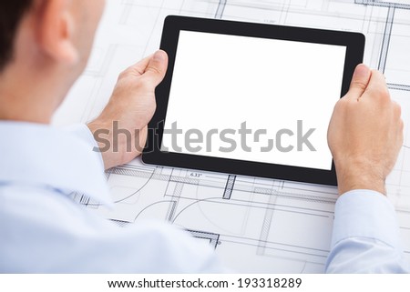 Cropped image of businessman holding blank digital tablet over blueprint in office
