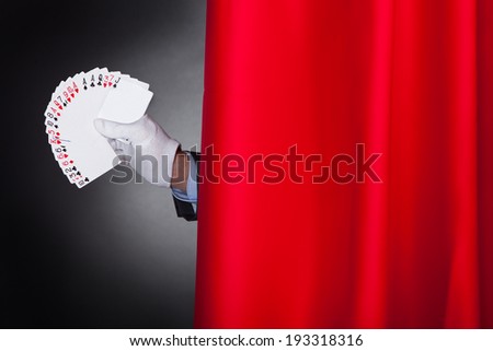 Cropped image of magician holding fanned cards behind stage curtain