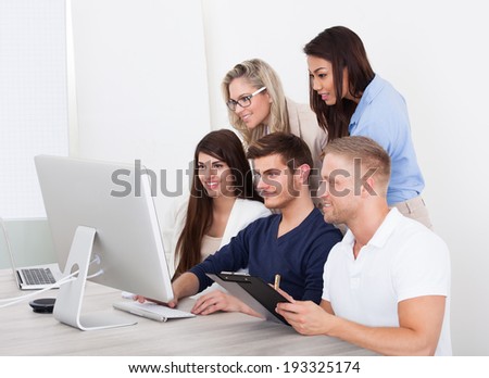 Group of smiling businesspeople using computer together in office